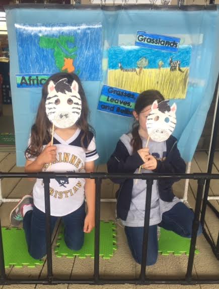 Two first grade students hold up the masks they made for the talking zoo.