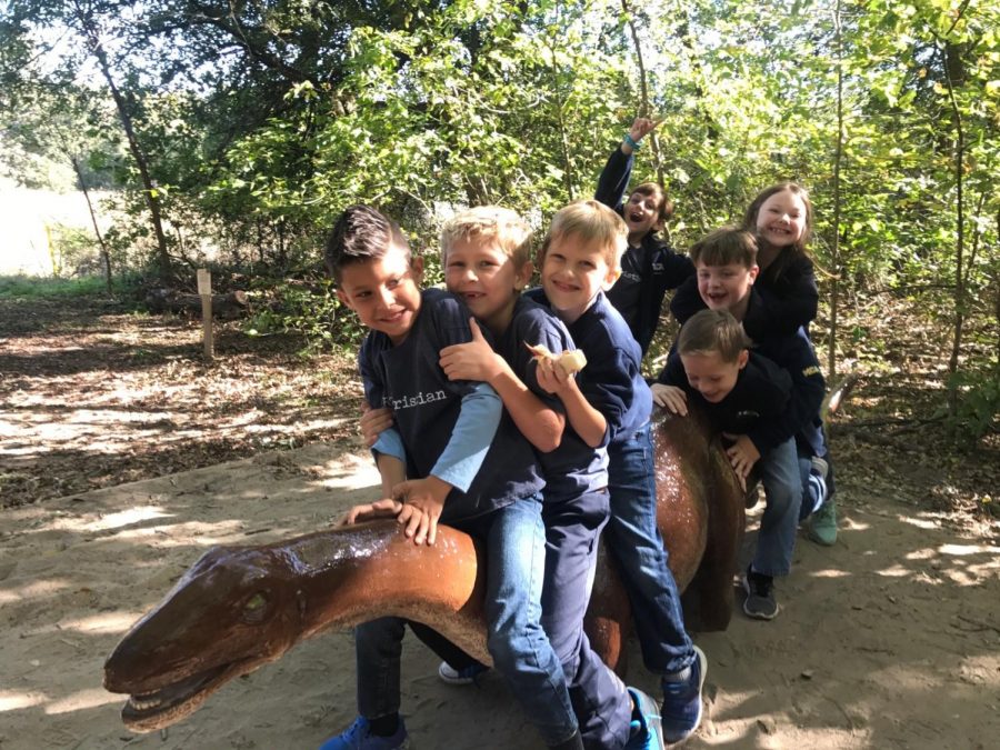 Some students take a sweet picture together on a statue dinosaur.