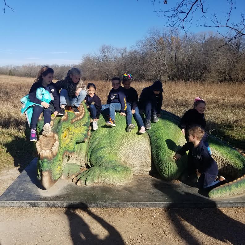 Second graders sit on top of a dinosaur statue. 