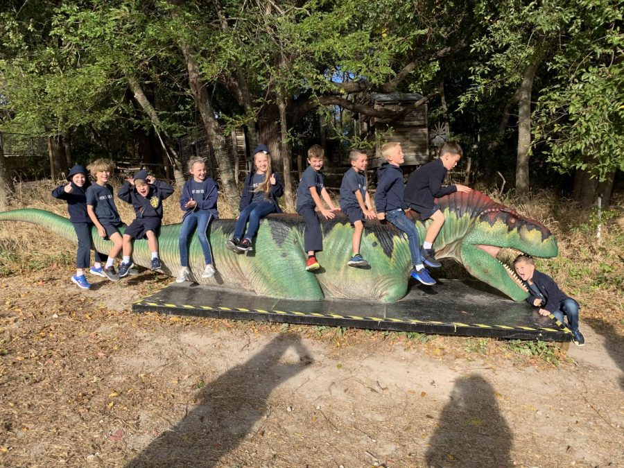 Second graders taking a picture while sitting on an electronic dinosaur.