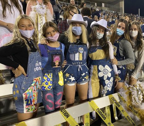 A group of senior girls posing for a picture in their senior overalls while cheering on their mustangs.