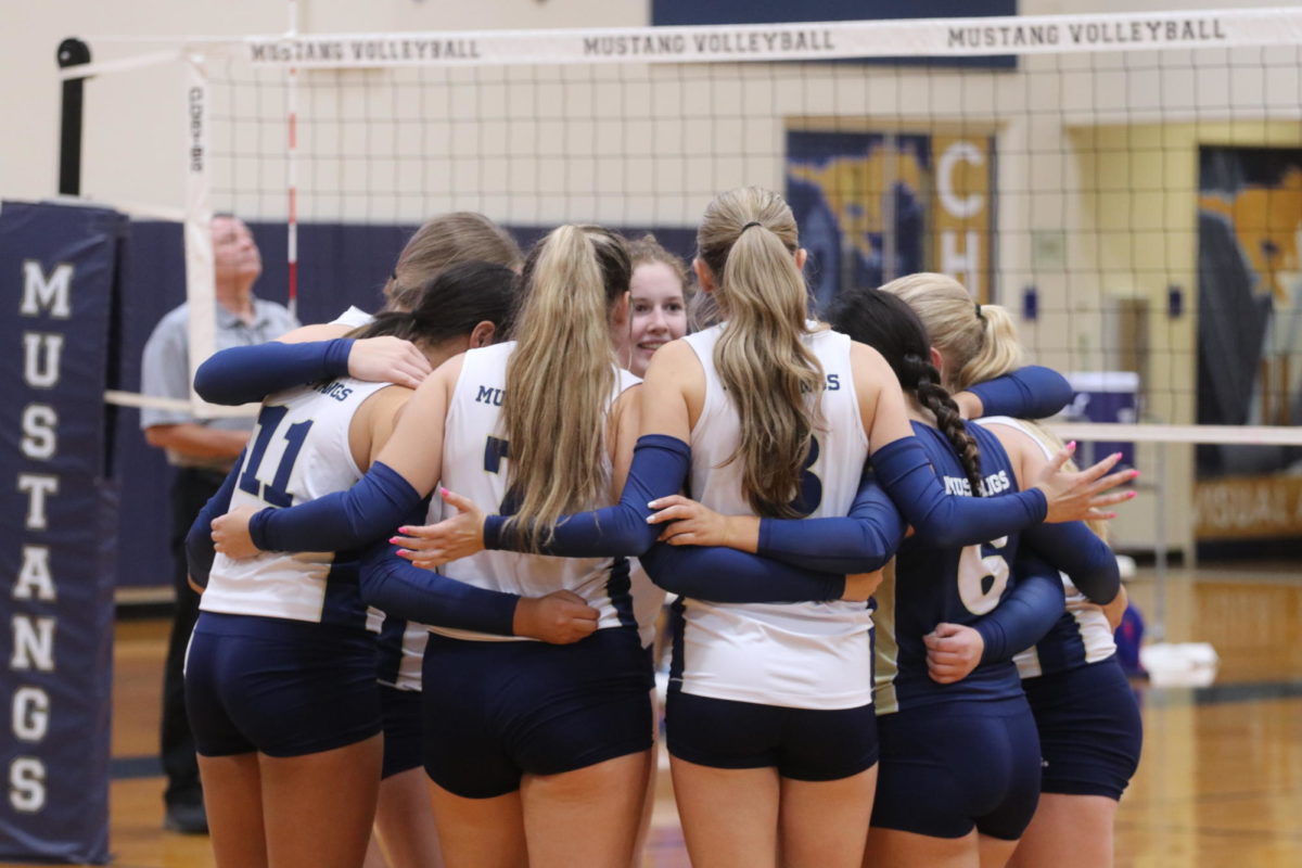 Varsity volleyball girls gather in a huddle.