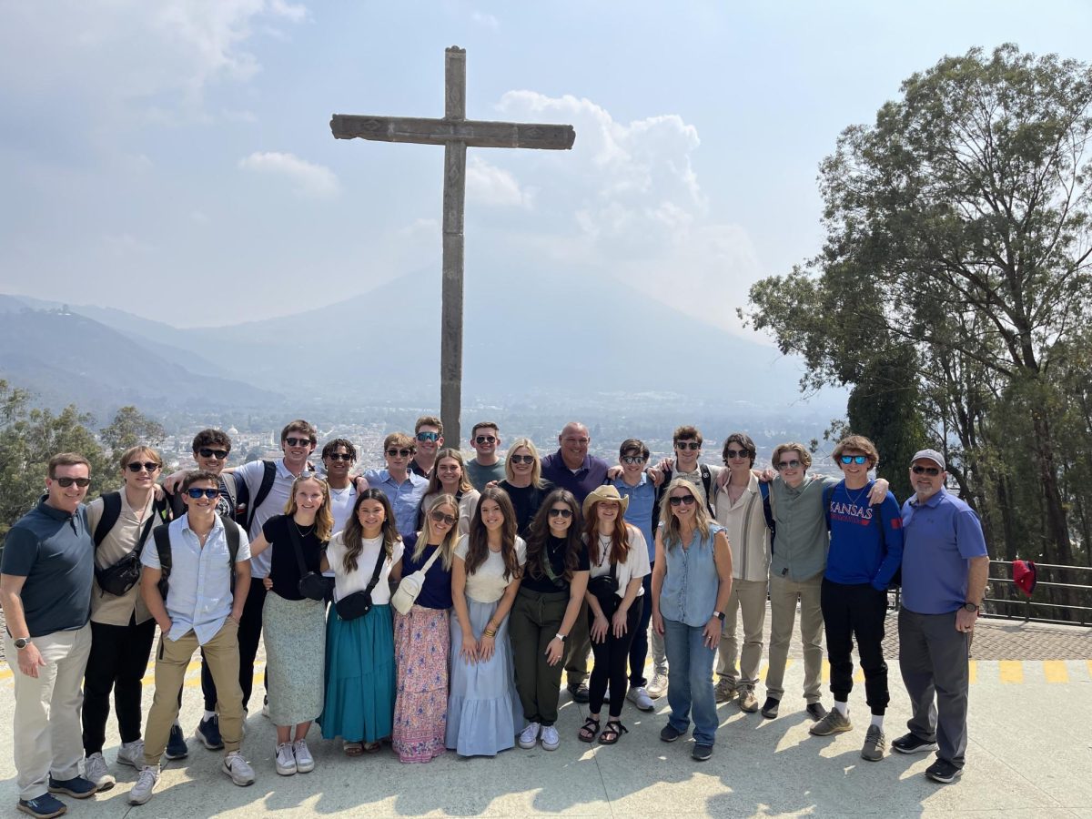 Students and chaperones on the trip pose for a picture next to a cross.